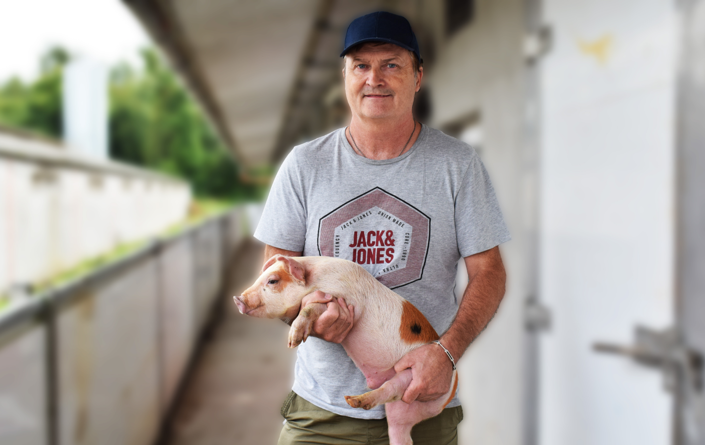 Farmer wearing cap and t-shirt holding a small brown mottled pig